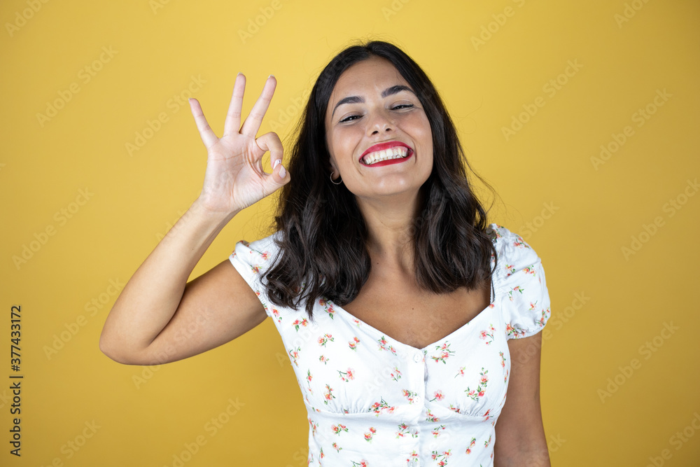 Beautiful woman over yellow background doing ok sign with fingers and smiling, excellent symbol Beautiful woman over yellow background doing ok sign with fingers and smiling, excellent symbol
