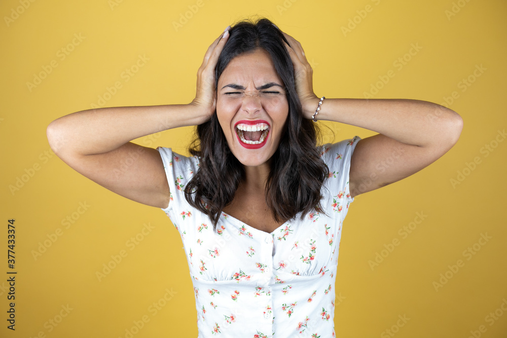 Fototapeta premium Beautiful woman over yellow background suffering from headache desperate and stressed because pain and migraine with her hands on head