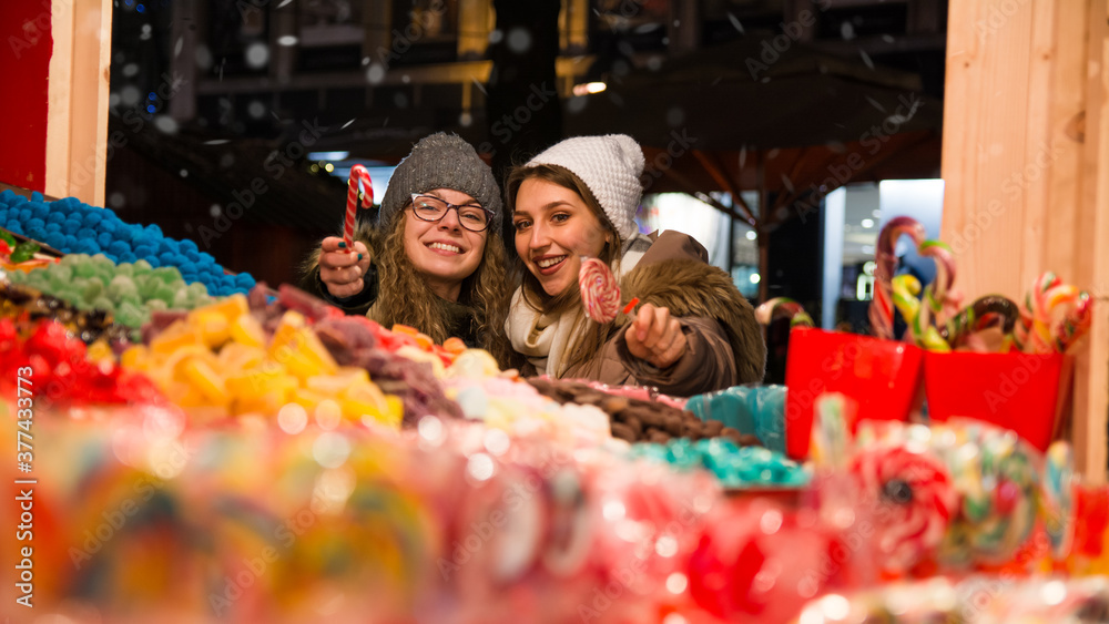 Smiling woman choosing candies with her female friend at the Christmas market