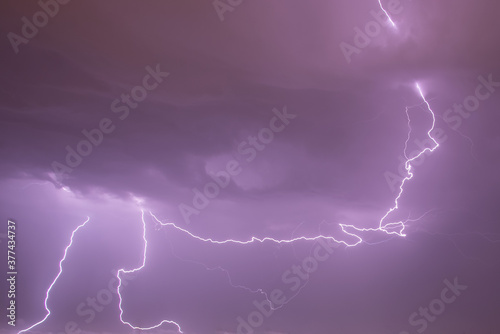 Forked lightning from a stormy sky with electric activity. Sky in purple (magenta) color.