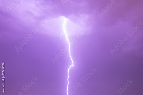 Straight down electric discharge coming from behind a cloud in stormy sky with lightning activity. Sky in purple (magenta) color. Staccato lightning.