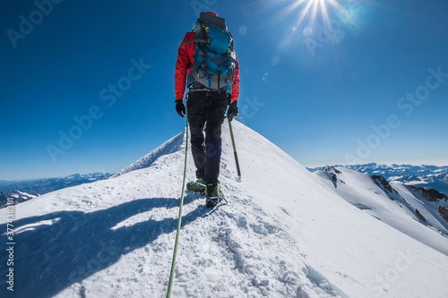 Backpack Last steps before Mont Blanc (Monte Bianco) summit 4,808 m of man  with climbing axe dressed mountaineering clothes, boots with crampons  walking by snowy slopes with blue sky background with bright