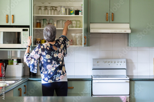Older woman reaching for water glass in kitchen cupboard