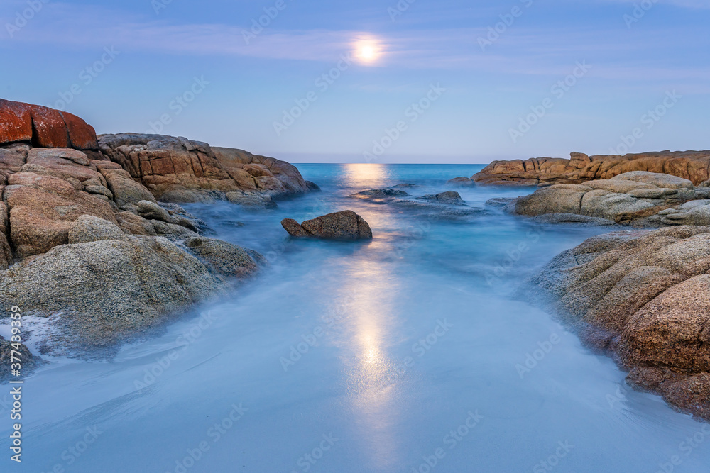 A full moon rising over an inlet along a rocky coastline A full moon rising over an inlet along a rocky coastline