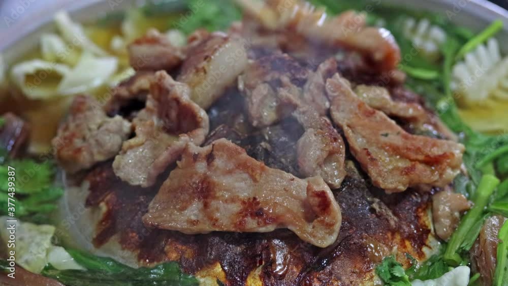 A preparation of roasted meat with sauce of vegetable on Hot Pot - Mu Kratha, close up..Grilled slice pork at Thai Barbecue style with smoke around. A preparation of roasted meat with sauce of vegetable on Hot Pot - Mu Kratha, close up..Grilled slice pork at Thai Barbecue style with smoke around.