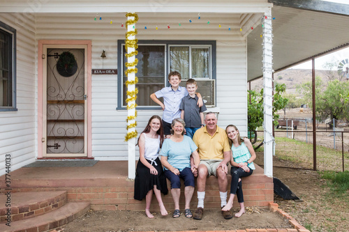 Retired grandparents sitting on front verandah of house with grandchildren happy photo