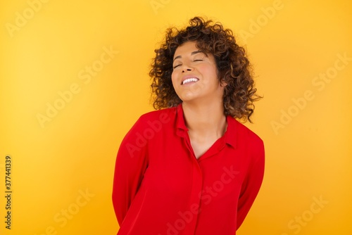 Young arab woman with curly hair wearing red shirt on yellow background very happy and excited about new plans.
