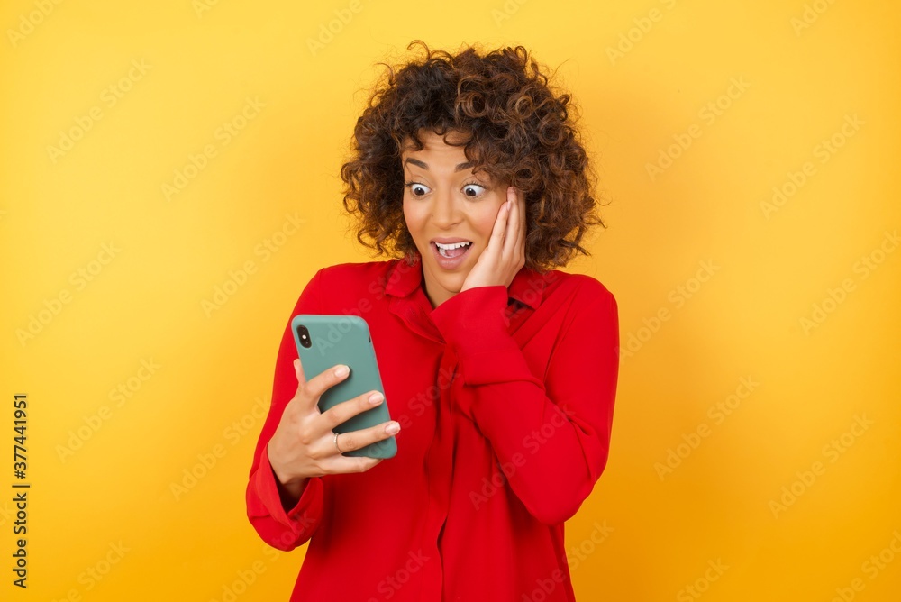 Close-up portrait of arab businesswoman holding in hands cell reading sms using new app 5g isolated on bright vivid shine yellow background Close-up portrait of arab businesswoman holding in hands cell reading sms using new app 5g isolated on bright vivid shine yellow background