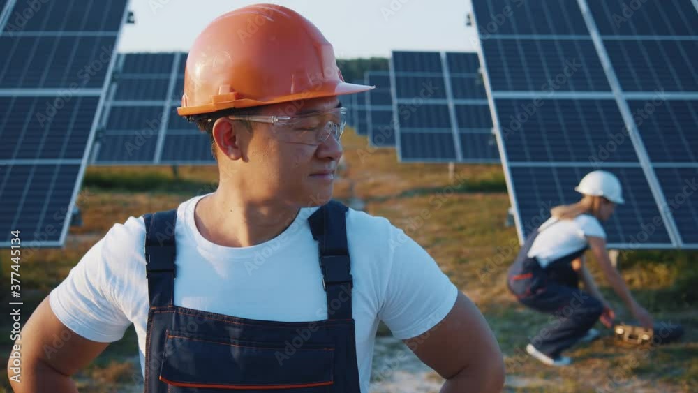 Portrait of cheerful adult asian enginner in industry uniform cooperating on ecological construction of solar farm outdoor. Workman. Renewable energy. Solar field. Portrait of cheerful adult asian enginner in industry uniform cooperating on ecological construction of solar farm outdoor. Workman. Renewable energy. Solar field.