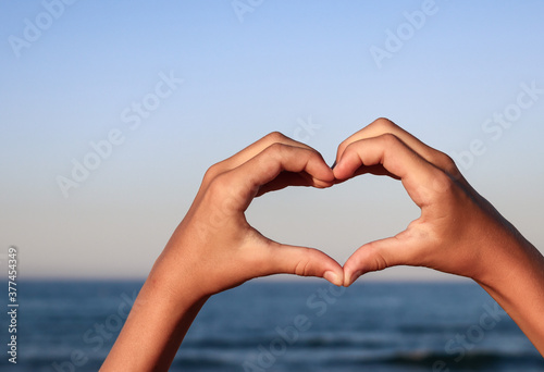 heart shape in hands. Heart shape in hands against a background of blue sea and with a place for text on the left  side view close-up.