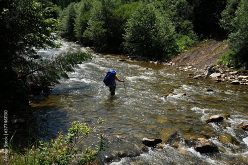 Hiker man hiking crossing river. Trekking journey and travel concept