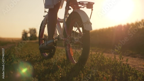 happy family in the park. Little girl rides a bicycle. The child's feet are pedaling. The kid is riding at sunset, spinning a bicycle wheel. A chidhood dream. Physical activity, cardio. photo