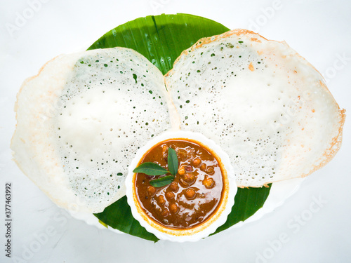Delicious appam/vellappam and peas curry/kadala curry decorated in a banana  plate with white background.