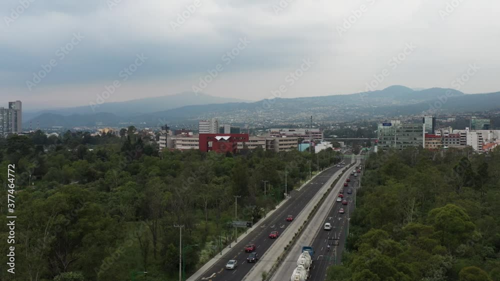 Vista aérea del tráfico sobre Av. Insurgente Sur a la altura del Centro Cultural Universitario  con el sur de la ciudad como fondo.