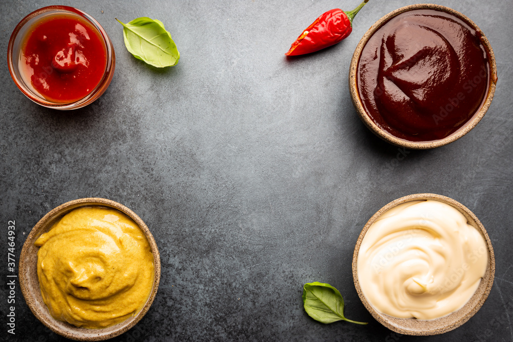 Classic set of sauces, American yellow mustard, ketchup, barbecue sauce, mayonnaise on black stone background, top view with copy space. Classic set of sauces, American yellow mustard, ketchup, barbecue sauce, mayonnaise on black stone background, top view with copy space.