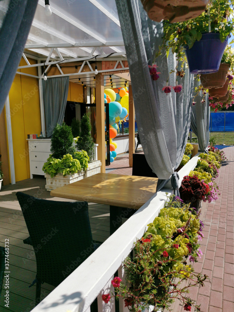 Empty outdoor cafe terrace. Opening. Tables and chairs with flowers under a canopy in a city park on a sunny hot day. Waiting for visitors