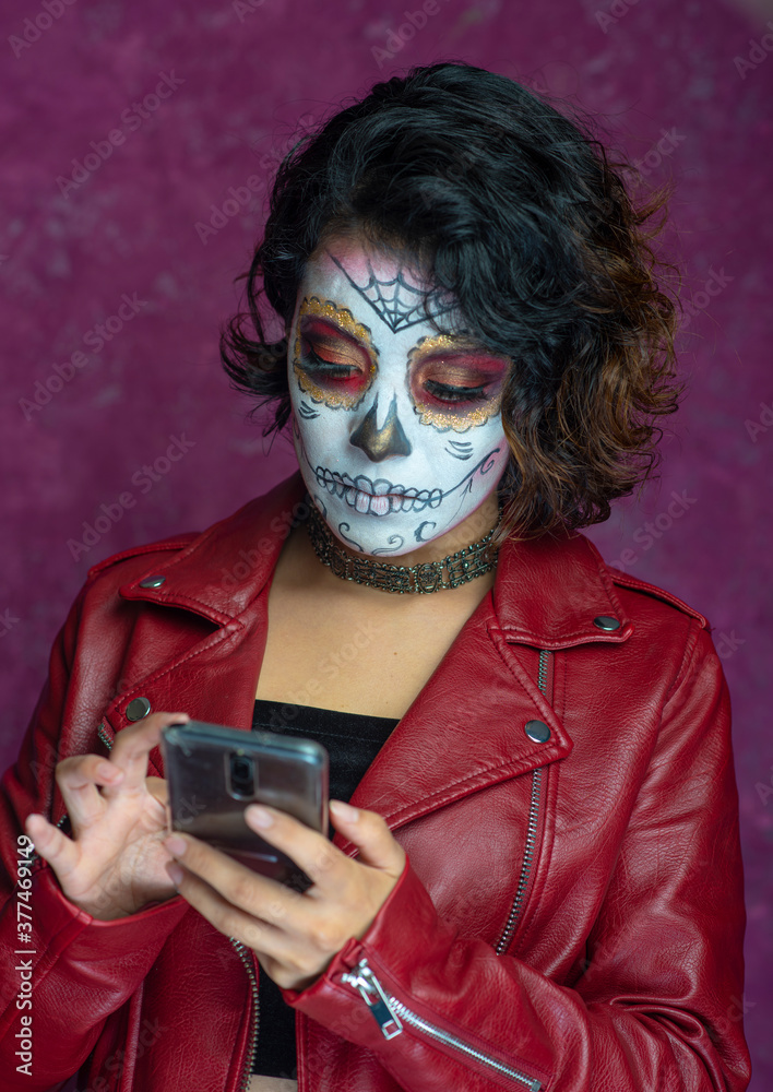 mujer joven latina mexicana smartphone celular texteando mensaje maquillaje catrina calavera día de muertos chaqueta roja cabello fondo rosa aislada foto de Stock | Adobe Stock