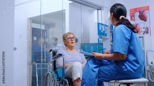 Handicapped senior woman in wheelchair talking with nurse in modern recovery clinic or hospital. Doctor help  assistance for disabled people with walking disability  medical care and treatment