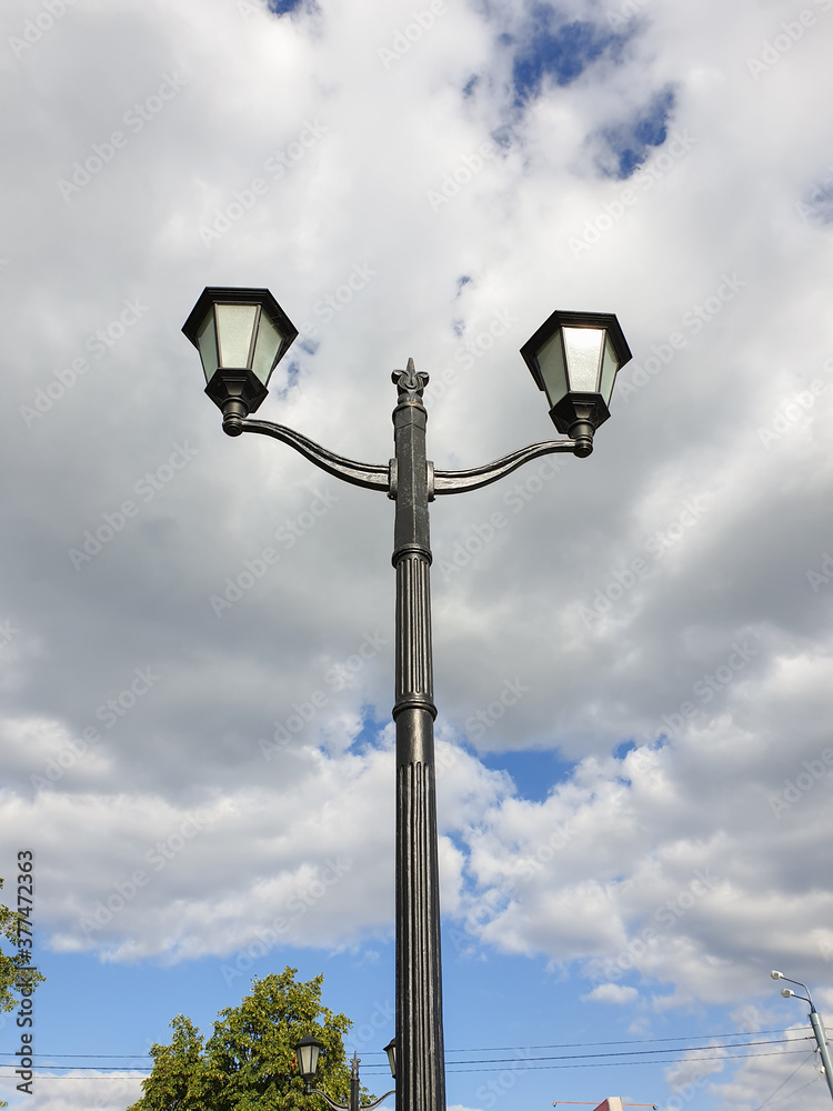 Street lamp on the background of the cloudy sky. In the town. Antique lamp. architectural European style. Street lights. Vertical photo.