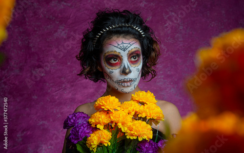 Mujer joven millennial bonita maquillaje catrina mexicana latina día de los muertos halloween calavera cara pintada festividad disfraces flores cempasuchil fondo rosa colorido punk moderna urbana