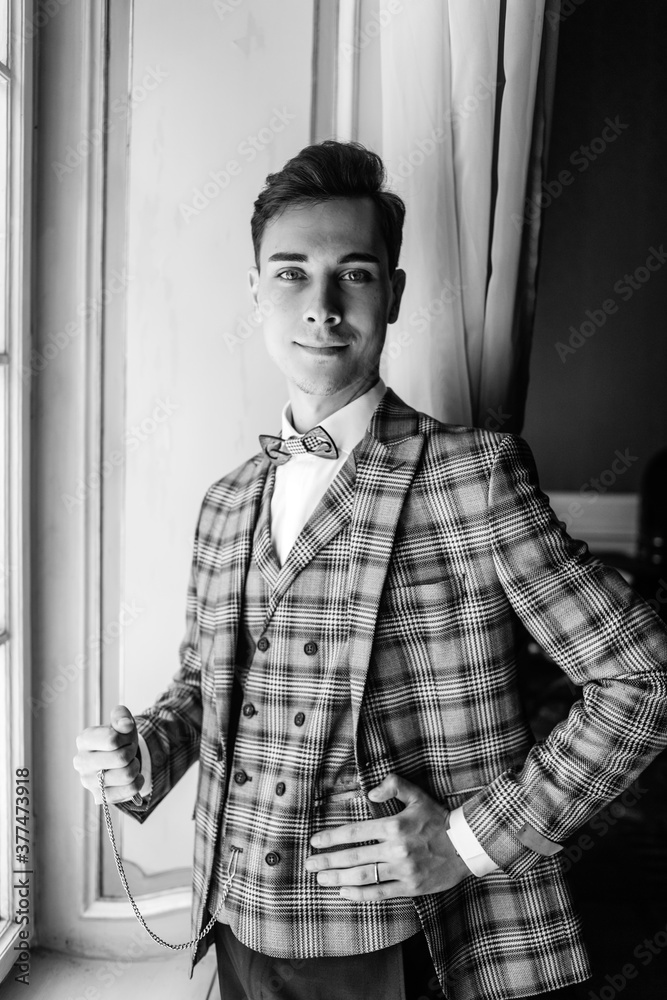 Black and white portrait guy in an elegant suit holding a watch in his hand, posing by the window. Black and white portrait guy in an elegant suit holding a watch in his hand, posing by the window.