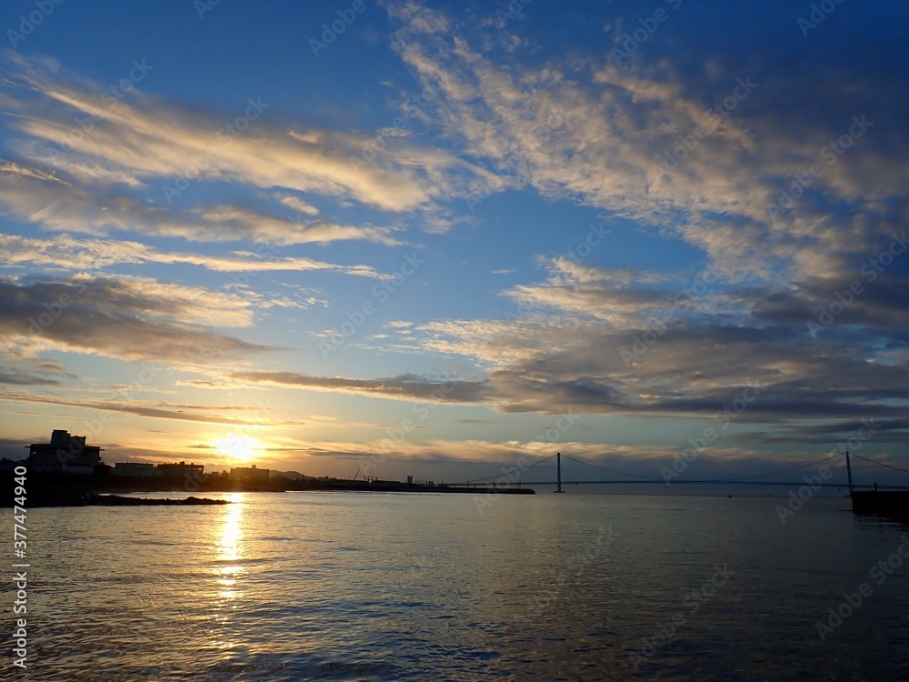 Naklejka premium 青空に輝く朝の太陽と、太陽に照らされた穏やかな海