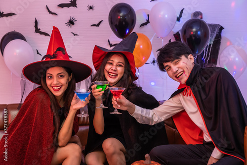 Young happy Asian people dressing Halloween costume, vampire and witch, celebrating in party. Holding and clinking wine glass. Looking at camera.