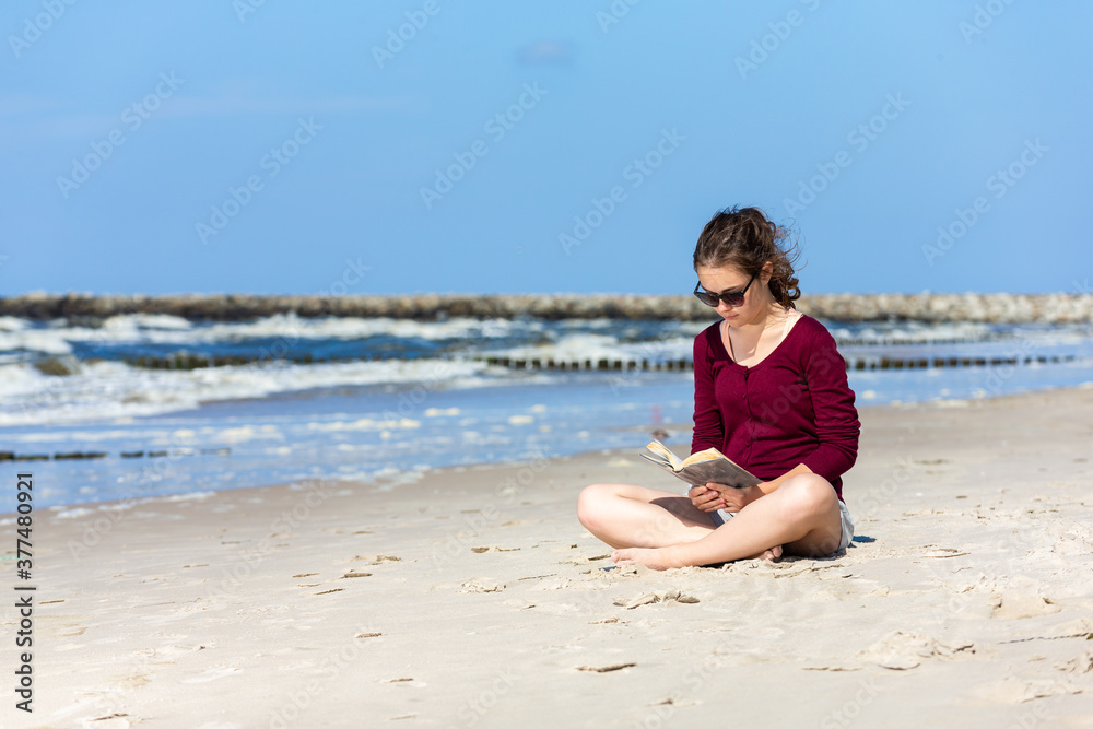 Teenage girl reading book sitting on beach