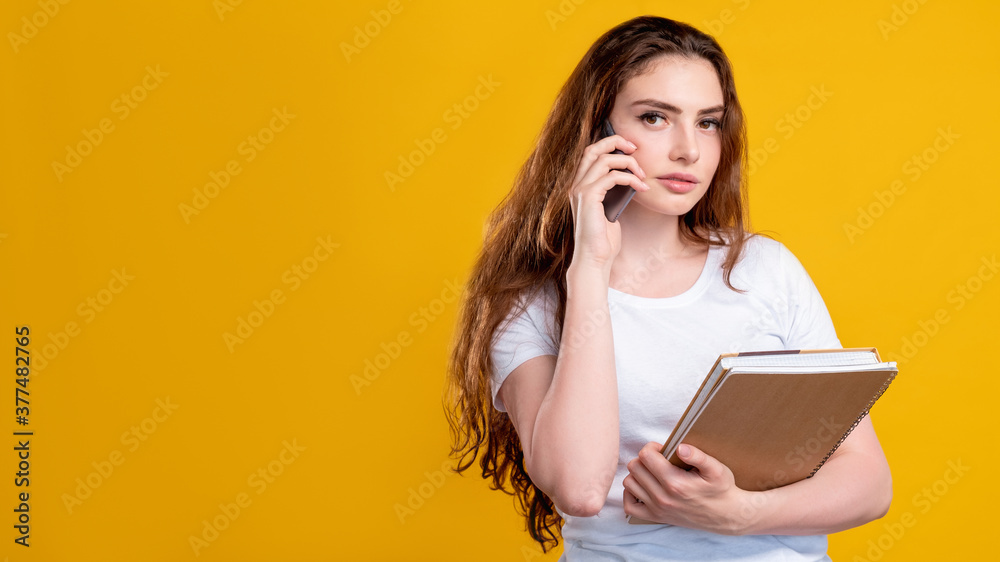 Business call. Mobile technology. Portrait of smart woman in white with notebooks talking on phone isolated on orange copy space background. Distance communication. Corporate life. Project management. Business call. Mobile technology. Portrait of smart woman in white with notebooks talking on phone isolated on orange copy space background. Distance communication. Corporate life. Project management.