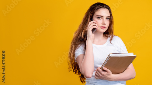 Business call. Mobile technology. Portrait of smart woman in white with notebooks talking on phone isolated on orange copy space background. Distance communication. Corporate life. Project management.