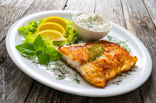 Fototapeta Naklejka Na Ścianę i Meble -  Fish dish - fried cod fillet with cream sauce and lemon served on wooden table
