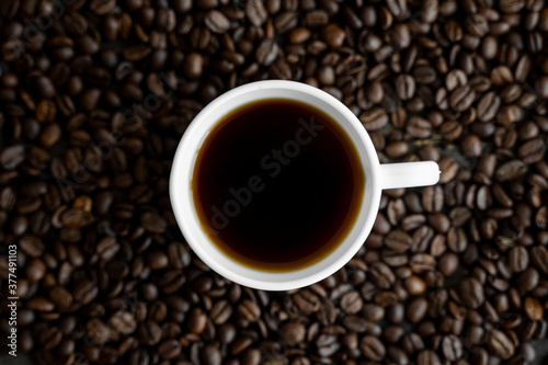 White cup of coffee with roasted coffee beans background. Mug of black coffee.