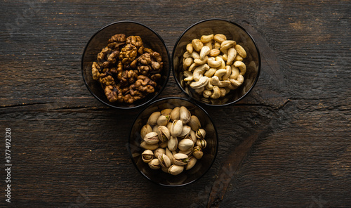 Walnut, pistachio and cashew in a small plates which standing on a black table. Nuts is a healthy vegetarian protein and nutritious food.