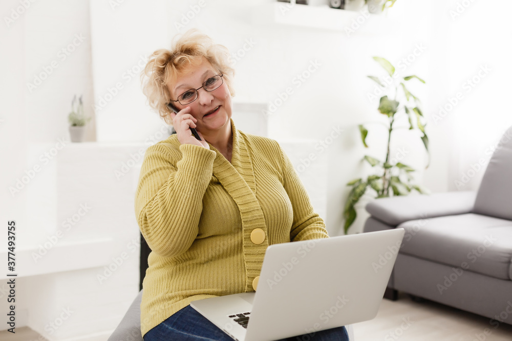 Attractive elderly woman sitting on couch at home, looking at camera, makes video call, communication distantly, modern wireless technologies concept Attractive elderly woman sitting on couch at home, looking at camera, makes video call, communication distantly, modern wireless technologies concept