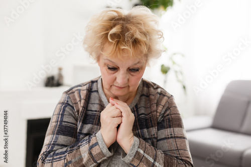 Religious faithful middle aged woman praying with hope faith holding hands clasped together in namaste at home in morning, old mature lady believer christian saying worship prayer
