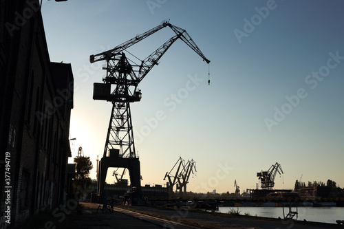 Silhouette of shipyard's tall crane. Industrial landscape - unused crane in formrer Gdansk Shipyard turned into sightseeing destination. Channels and other cranes in the background.