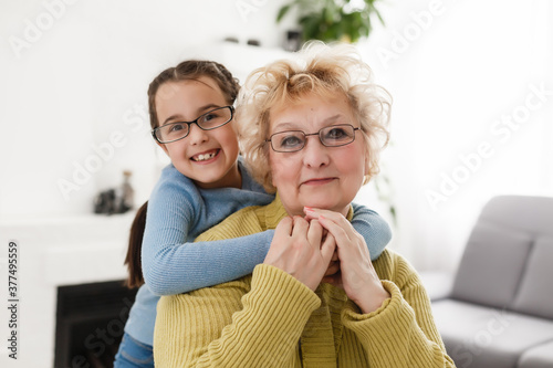 Portrait of happy old grandmother and kid girl looking at camera, smiling grandma with granddaughter making video call, child and granny vloggers recording video blog or vlog together