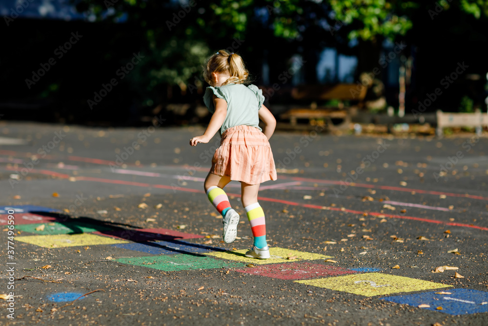 Naklejka premium Cute little toddler girl playing hopscotch game drawn with colorful chalks on asphalt. Little active child jumping on playground outdoors on a sunny day. Summer activities for children.