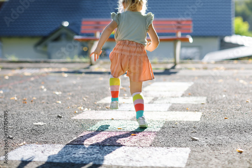 Closeup of leggs of little toddler girl playing hopscotch game drawn with colorful chalks on asphalt. Little active child jumping on playground outdoors on a sunny day. Summer activities for children. photo