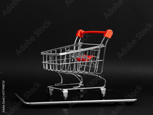 A tablet and shopping cart on a black background, a blank for the design, concept. Copy space.