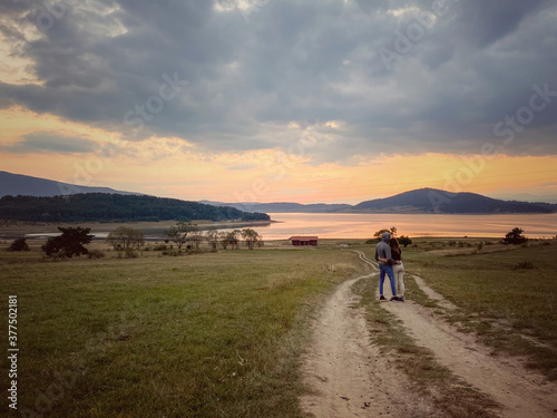 Two persons are watching the scenic sunset near the dam.