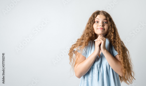 Photo of charismatic young woman with curly long hair keeps hands together near chin, has cute expression. Copy space