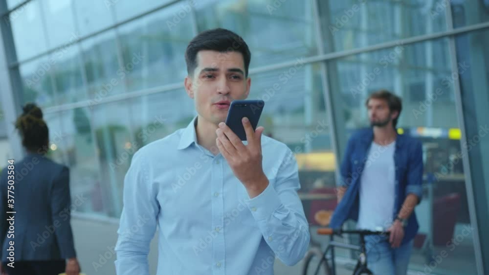 Caucasian attractive businessman holding cellphone communicating with colleague through audio messages recording voice sms on application outdoors. Caucasian attractive businessman holding cellphone communicating with colleague through audio messages recording voice sms on application outdoors.