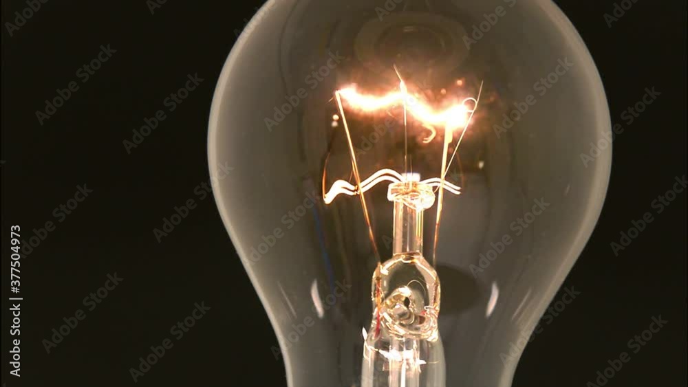 Close-up of electrified tungsten light bulb glowing in black background