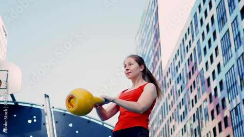 Young female athlete doing workout, training with a kettlebell in the open air. photo