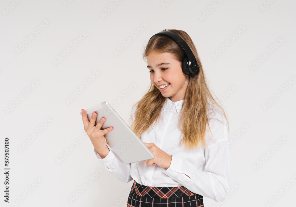 Cute smiling teen girl in school uniform with headphones and tablet in her hands isolated on the white background Cute smiling teen girl in school uniform with headphones and tablet in her hands isolated on the white background