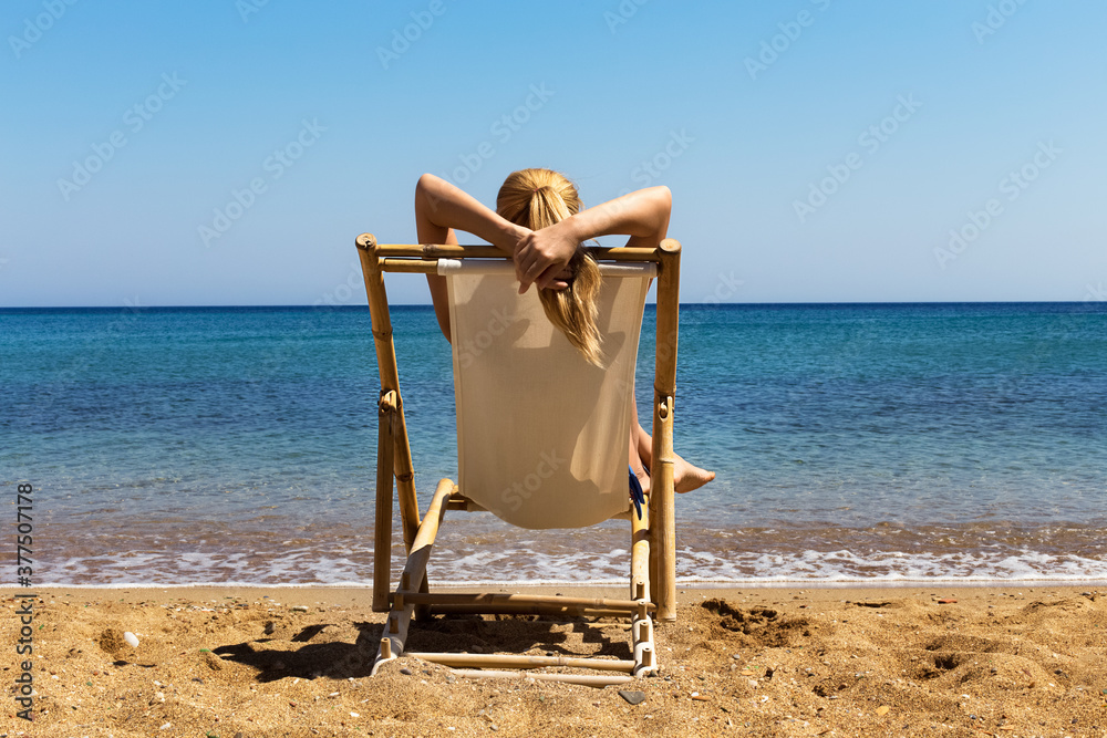 Beautiful young blond woman sitting in beach chair at the beach. Travel and lifestyle concept Beautiful young blond woman sitting in beach chair at the beach. Travel and lifestyle concept