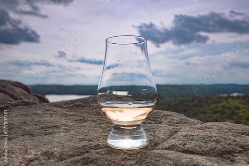 Принти на полотні A glencairn glass with a dram of scotch whisky siting on a cliff overlooking a valley of trees and lakes