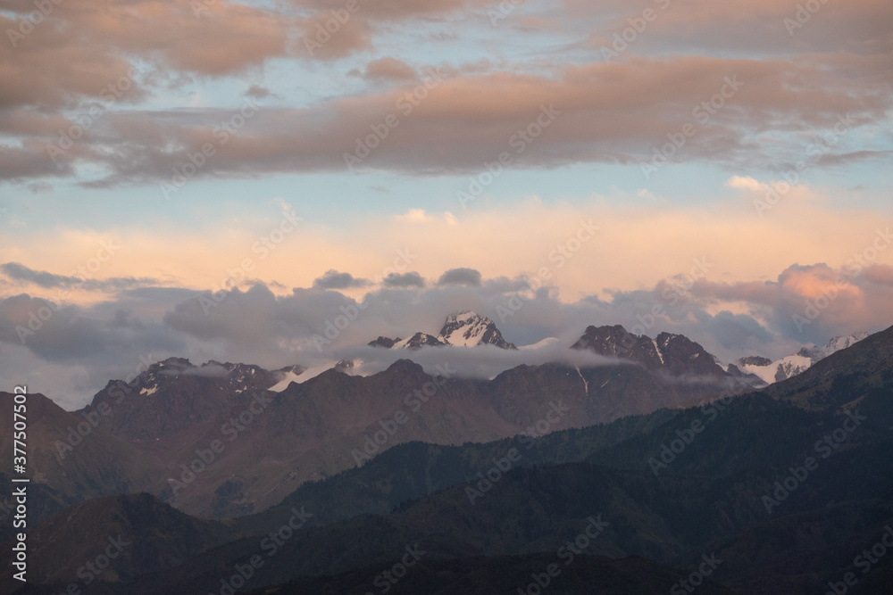 Sunset over the mountains, peaks covered with clouds, scenic sky 