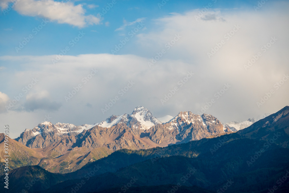 Peaks of mountains and glaciers in the clouds, blue sky